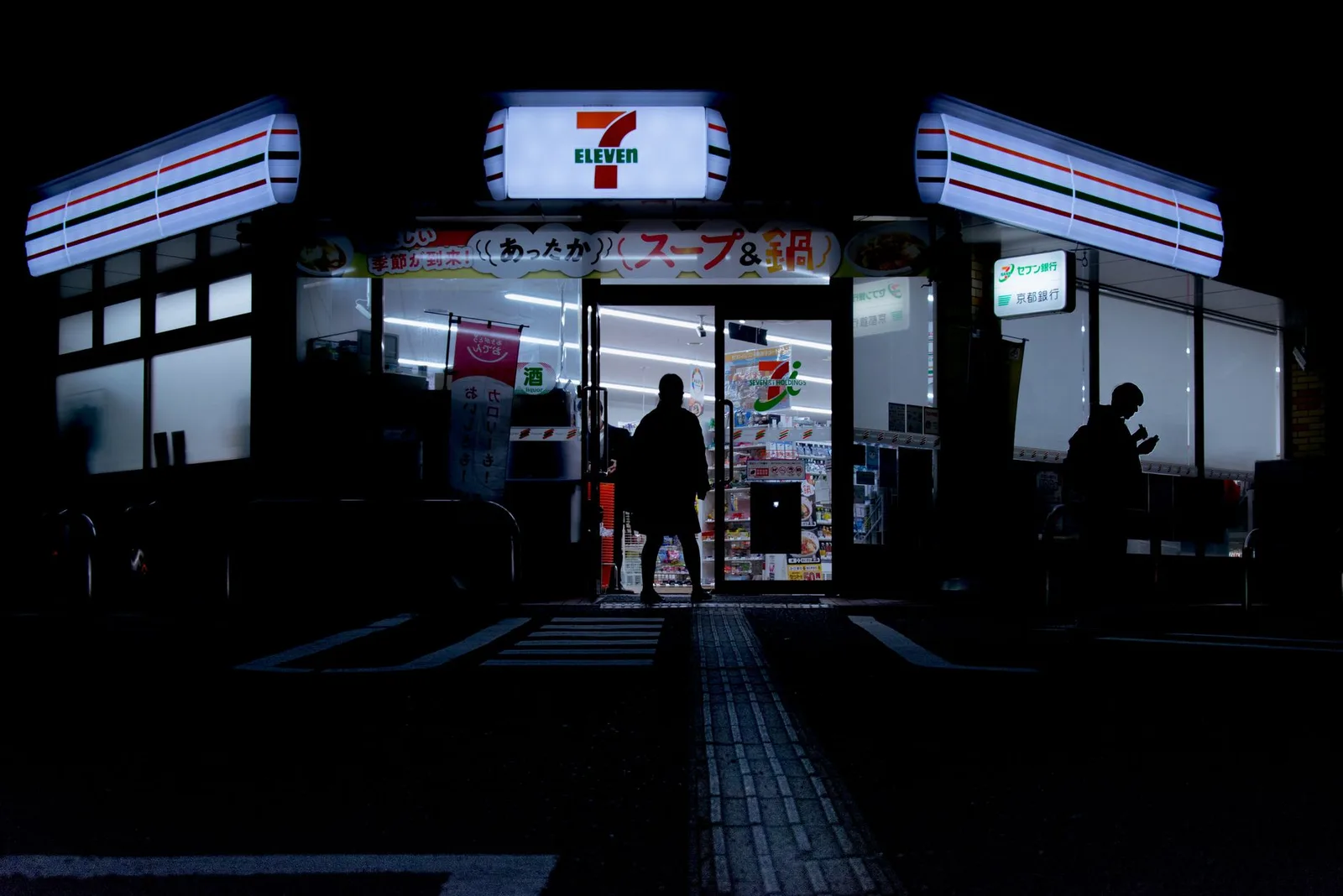 חזית חנות קומביני 7-Eleven מוארת בלילה ברחוב ביפן עם מדפי אוכל מלאים ושלטים בכתב יפני