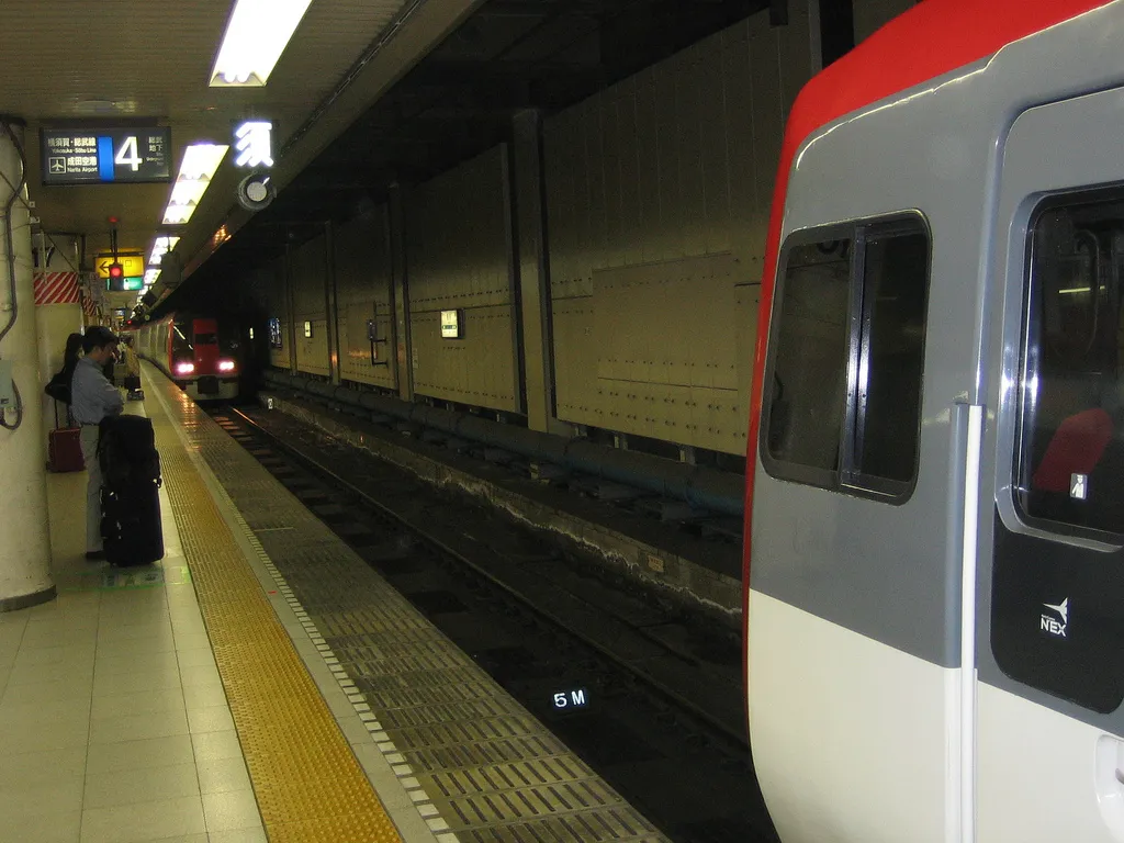 רכבת Narita Express האדומה לבנה בתחנה ביפן, הרכבת המהירה משדה התעופה נריטה למרכז טוקיו